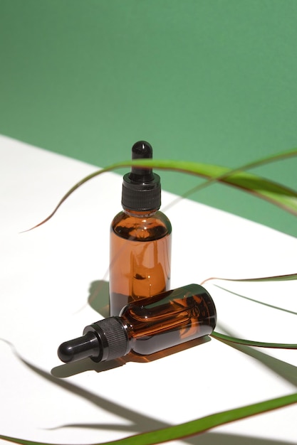 Amber glass dropper bottles different sizes with leaves on white green background Hyaluronic acid oil serum with collagen and peptides skin care product