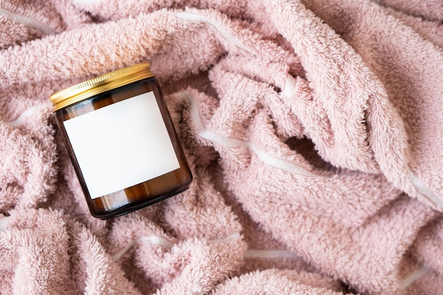 Amber glass jar with metal lid and white blank label on pink cotton fabric background