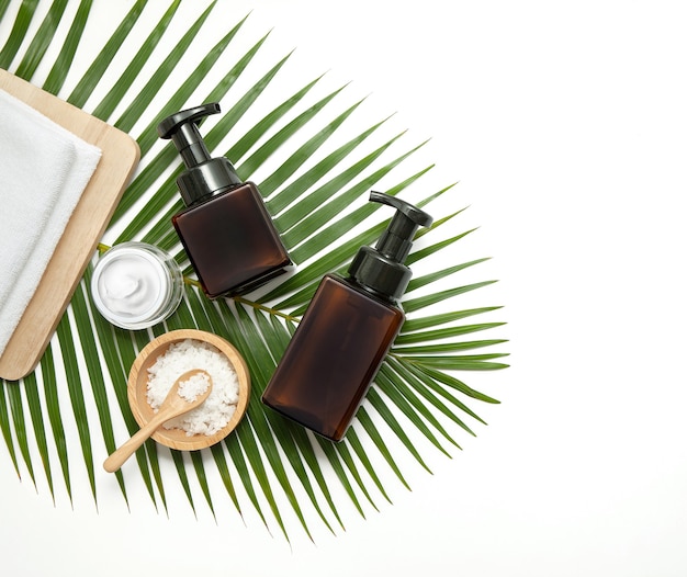 Amber glazen cosmetische flessen met spa-element en handdoek met groen blad op marmeren achtergrond. Plat lag, bovenaanzicht.