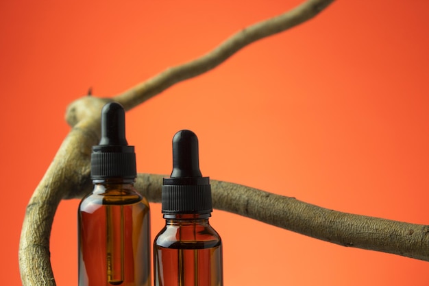 Amber glazen druppelflesjes met etherische olie of serum SPA natuurlijke biologische cosmetica verpakkingsontwerp Boomtak op oranje achtergrond