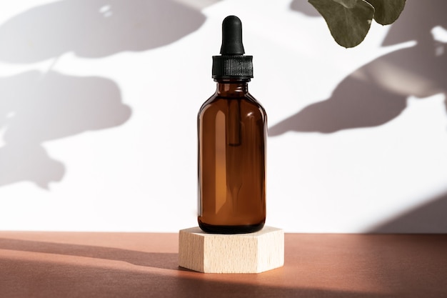 Amber serum cosmetic bottle on wooden geometric pedestal podium, product packaging with natural shadows from plants, anti aging serum with peptides, cosmetics, skincare concept. Front view