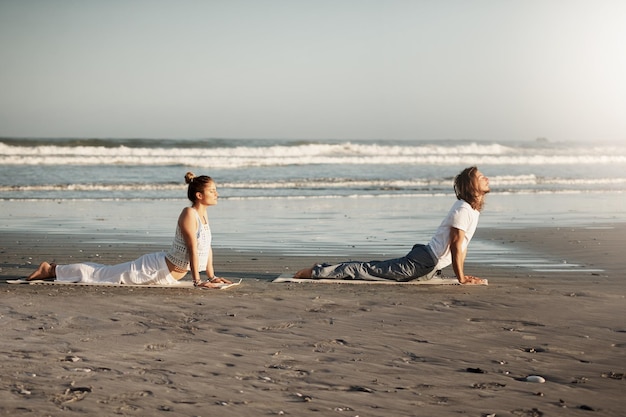 The ambience of the area will add to your yoga Shot of a young couple practising yoga together on the beach