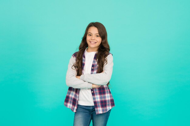 Ambitious and beautiful schoolgirl has long curly hair child in trendy casual jacket kid spring and autumn fashion little beauty express positive emotions happy small girl turquoise background