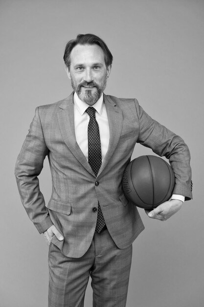 Ambitious coach business coach hold basketball ball basketball\
coach grey background confident coach or teacher in formalwear\
strategy and management professional at training