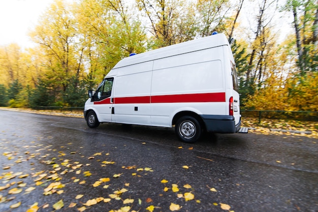 Ambulance passing by at the street in autumn. Rainy day