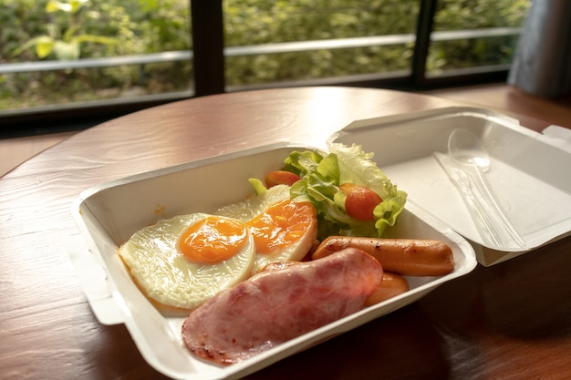 American breakfast meal style in a paper box set. small meal of\
hams and fried eggs.