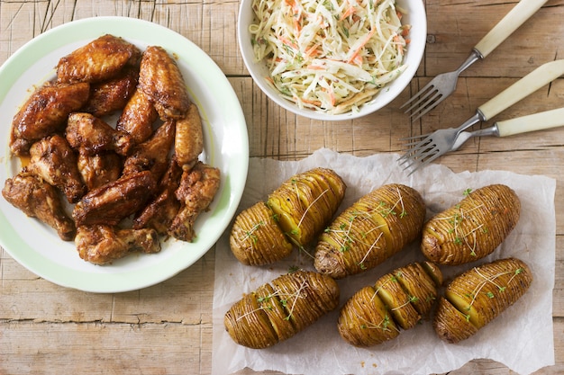 American chicken wings, hasselback potatoes with sauce and coleslaw on a wooden background. Rustic style.