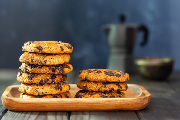 American cookies met stukjes chocolade op een houten bord en een koffiepot op een tafel