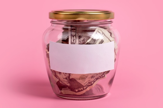 Photo american dollar bills in glass money jar with blank label on pink background