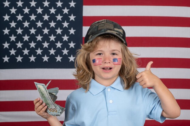 Foto sogni americani kid con centinaia di dollari di denaro isolato su sfondo studio bambino con il giorno dell'indipendenza della bandiera americana 4 luglio concetto degli stati uniti d'america