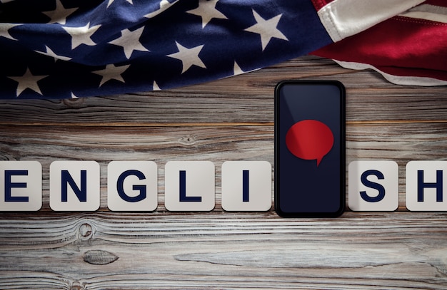 American English language Concept. Mobile Phone with Speech Bubble and USA Flag lay on Vintage Wooden background. Online Learning. Speak English. Top View