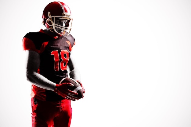 American football player in helmet holding rugby ball with hand raised