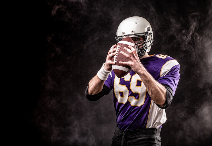 Photo american football player holding ball in his hands in smoke. black wall, copy space. the concept of american football, motivation, copy space