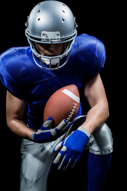 American football player holding ball while kneeling