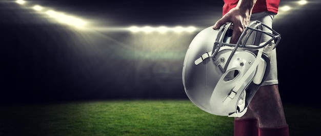 American football player holding helmet against rugby stadium