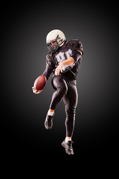 American football player in a jump with a ball on a black background