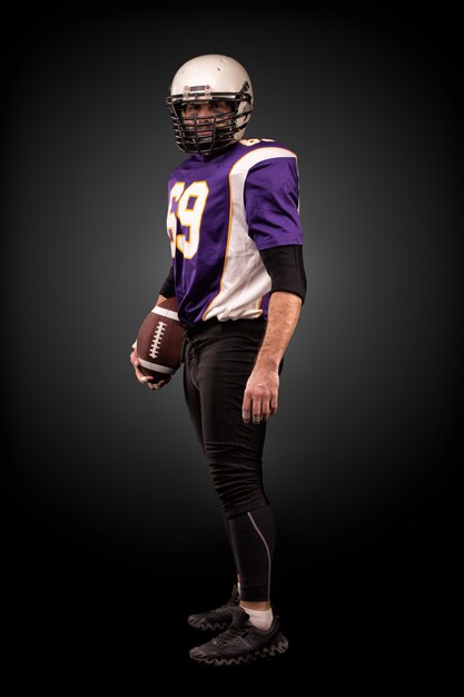 American football player posing with ball on black wall