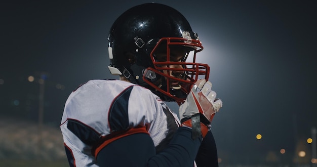 American football player putting on his protective helmet against bright stadium illumination lights