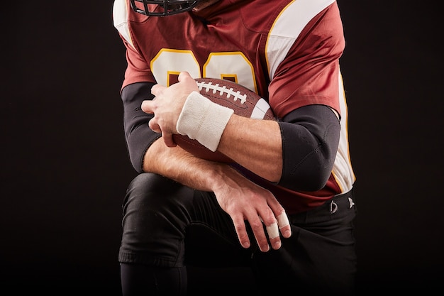 Photo american football player sitting in a position of readiness, hands to keep a mache on a black background, concept