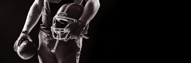 American football player standing with helmet and rugby ball