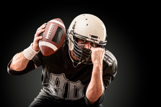 American football-speler in donker uniform met de bal bereidt zich voor op de aanval