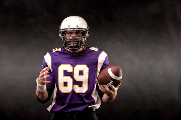 American football-speler poseren met bal op zwarte achtergrond