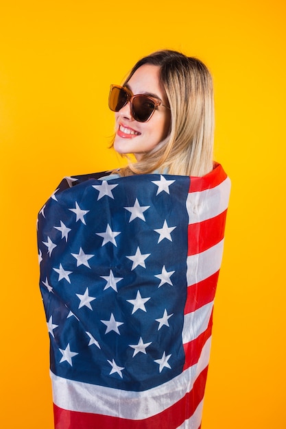 American girl drapes herself with a large American flag on yellow background.