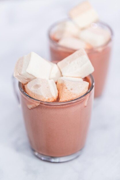 American hot chocolate topped with large marshmallow in glass cup.