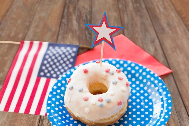 american independence day, celebration, patriotism and holidays concept - close up of glazed donut with american flag and star decoration on disposable plate at party over wooden table background
