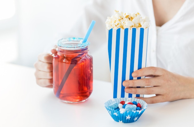 アメリカの独立記念日、お祝い、愛国心、祝日のコンセプト – 7月4日のパーティーでガラス製のメイソンジャーに飲み物とキャンディーを入れてポップコーンを食べる女性の接写