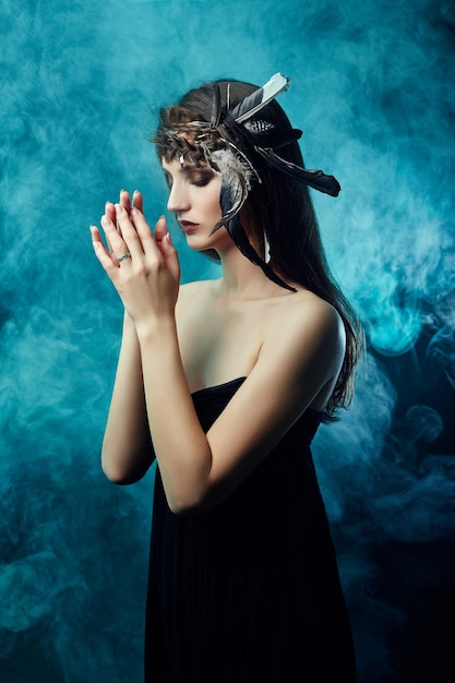 American indian girl with feathers in her hair and makeup on\
her face in blue smoke