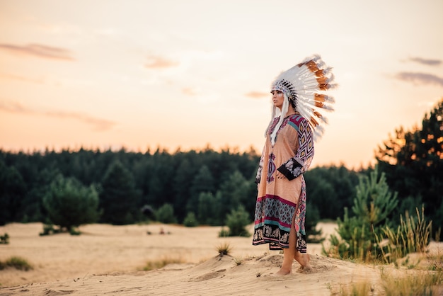 Фото Женщина американских индейцев смотрит вдаль на открытом воздухе. чероки, культура навахо. головной убор из перьев диких птиц. традиционный костюм
