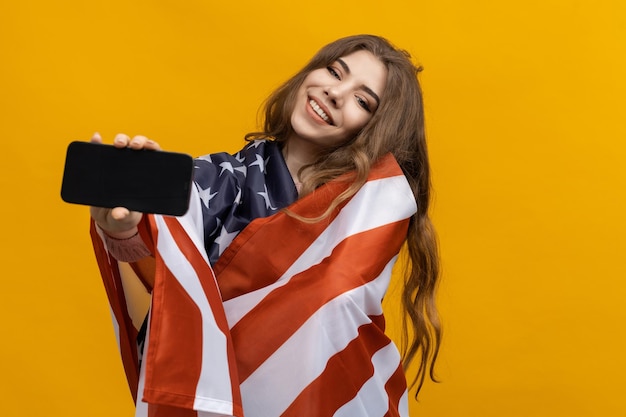 An American IT startup A smiling woman holds out her hand to the camera with a smartphone on a yellow background