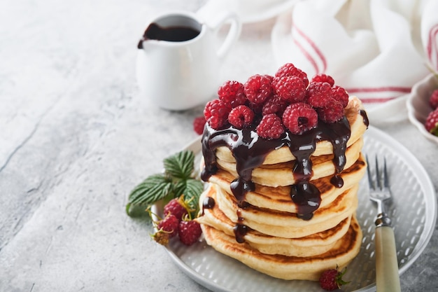American pancakes Stack pancakes with fresh raspberry with chocolate glaze or toppings in white bowl on light gray table background Homemade classic american pancakes Magazine concept Top view