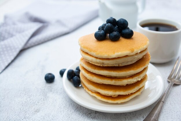 Pancake americani con i mirtilli, la prima colazione o lo spuntino, isolati su bianco