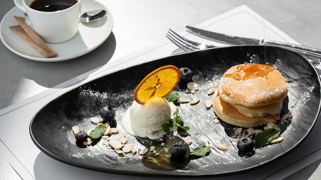 American pancakes with ice cream scoop, berries and maple syrup on black plate isolated with coffee. cafe menu