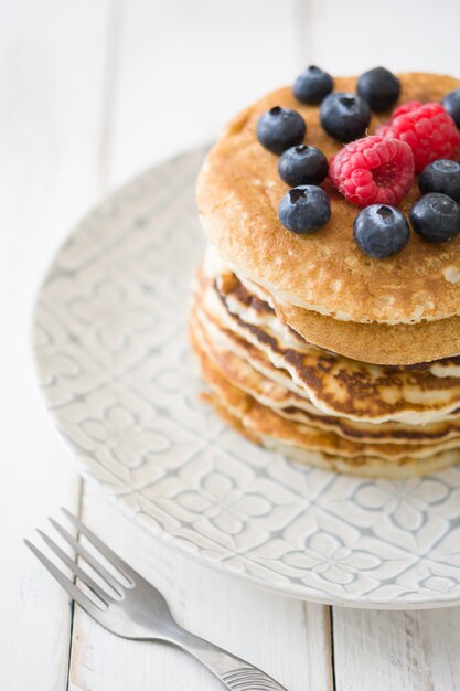 American pancakes with raspberries and blueberries on white wooden table