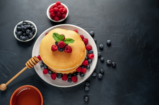 American pancakes with raspberries, fresh blueberries and honey. Healthy breakfast on concrete