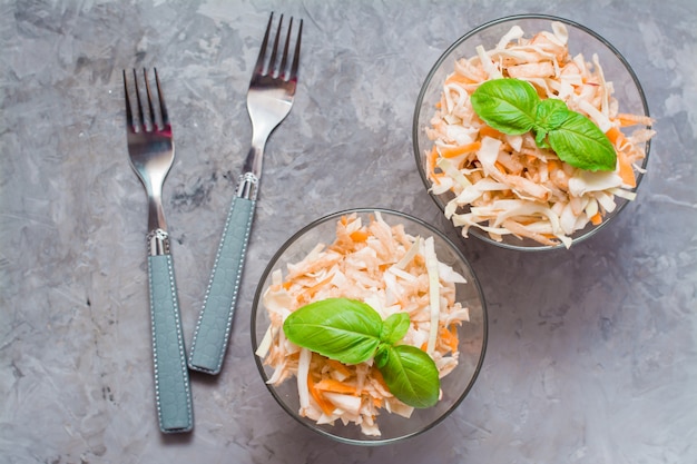 American ready-to-eat cole slaw salad of cabbage, celery, carrots and apples with basil leaves in glass bowls in the ingredients for cooking on the table. The concept of healthy and proper nutrition