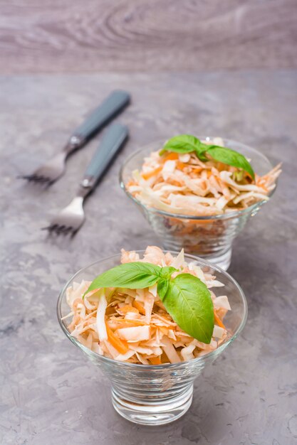 American ready-to-eat cole slaw salad of cabbage, celery, carrots and apples with basil leaves in glass bowls on the table.