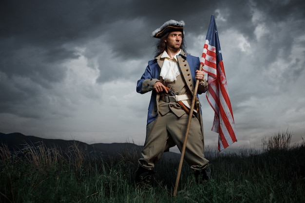 American revolution war soldier with flag of colonies over dramatic landscape