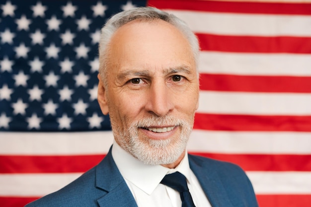 American senior man politician looking at camera with American flag on background Election day