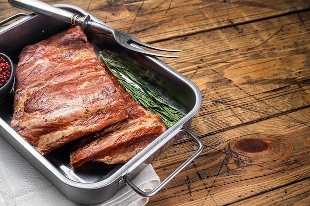 American Smoked Pork spare Ribs in steel tray with herbs Wooden background Top view Copy space