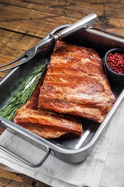 American Smoked Pork spare Ribs in steel tray with herbs Wooden background Top view