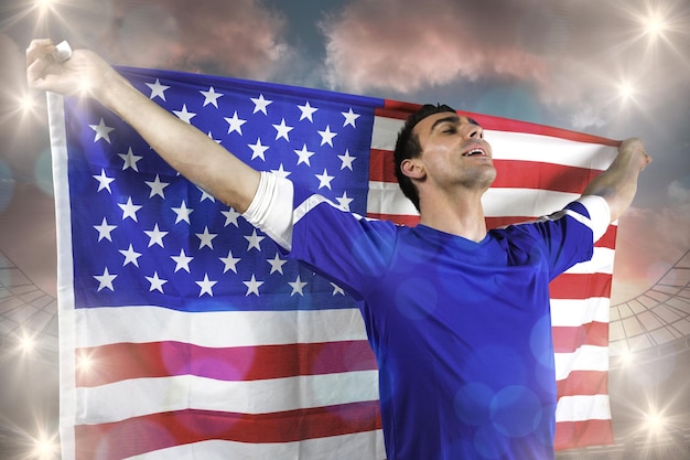 Американский футбольный фанат держит флаг против большого футбольного стадиона под облачным голубым небом