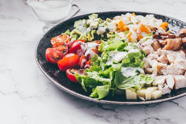 American traditional Cobb salad with chicken, avocado, tomatoes, eggs, bacon and cheese  on a marble table top view.