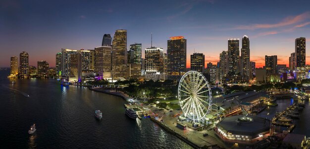 American urban landscape at night Skyviews Miami Observation Wheel at Bayside Marketplace with reflections in Biscayne Bay water and high illuminated skyscrapers of Brickell city's financial center