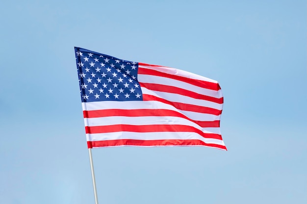 American USA flag red white and blue stars and stripes blowing in the wind on a flagpole against blue sunny skies celebration of Independence Day in the USA