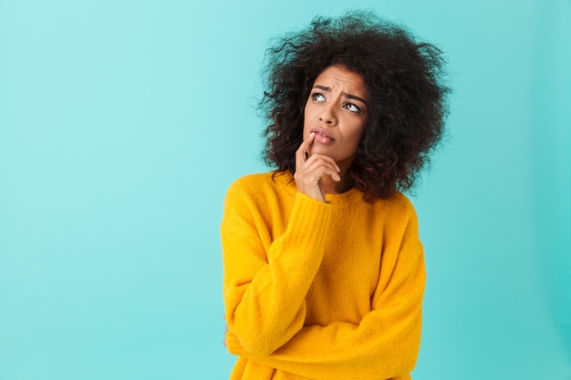 American woman in colorful shirt looking upward remembering or reflecting, isolated over blue wall