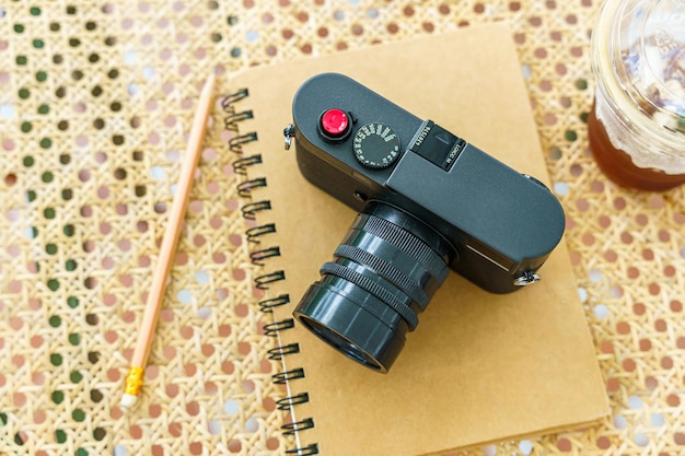 Americano iced coffee or black coffee in cup mug and camera in notebook on wood desk on top view As breakfast In a coffee shop at the cafeduring business work concept